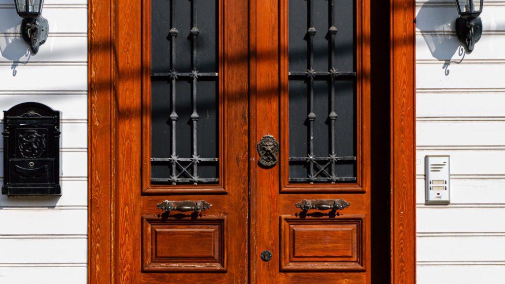 Elegant wooden entrance door with glass panels and flanking wall lights