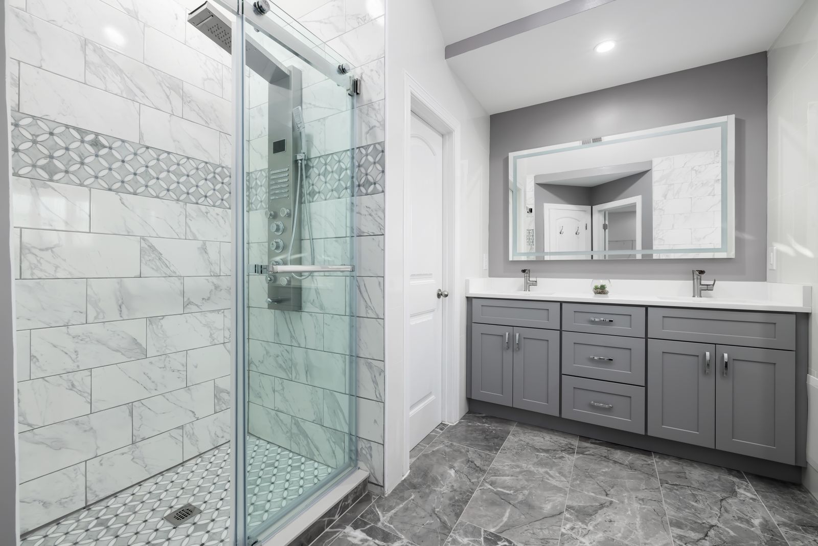 Bathroom with grey vanity cabinets and marble-tiled shower
